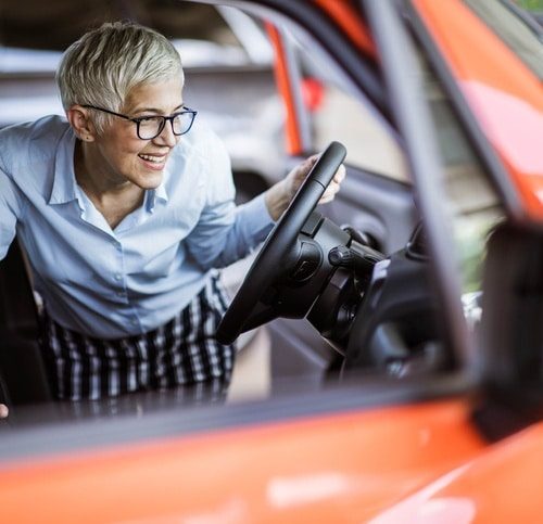 Happy mature woman buying a car in a showroom.