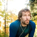Young handsome runner with earphones outside in autumn nature