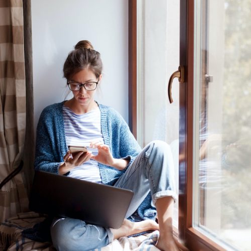 Young woman working from home office. Freelancer using laptop, phone and the Internet.