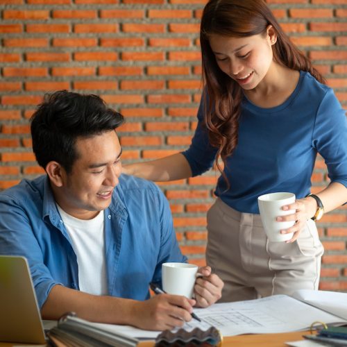 Asian architecture or engineer discussing with his partner in office with laptop, lifestyle concept.  Brick wall background.