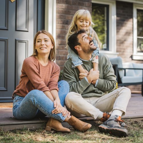 Young family with little girl having fun in front of there house. Porch is decorated with flowers.