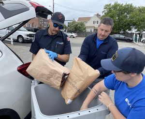 Three people emptying paper bags into a bin.
